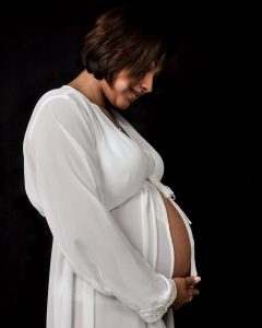 Retrato de una mujer embarazada en su sesión de fotos de maternidad. Viste ropa cómoda y elegante, resaltando su figura. Fondo neutro de estudio. Fotografía profesional por Click Fotografía.
